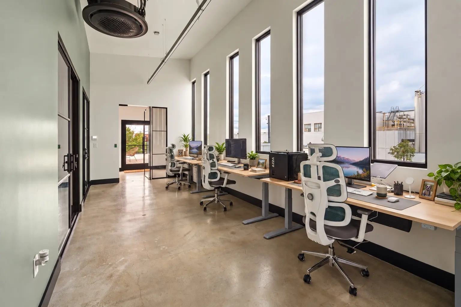 Fixed desks set up with monitors along a row of tall windows on the second floor